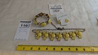 Yellow-themed costume jewelry including necklace, bracelet and earrings laid on white fabric with measuring tape to show size.