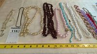 Photo of 12 costume jewelry necklaces laid out on a table with tape measure to show lengths ranging from about 7 to 18 inches.