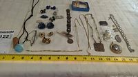 Wide view of the collection of various costume jewelry including earrings, bracelets, necklaces, and pins arranged on a white surface with a ruler for scale.