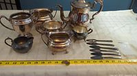 Full view of the silverware tea set on a table with a measuring tape showing length approx 16 inches for the largest piece.