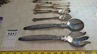 Photo showing full set of eight silver plated serving utensils, including large serving spoon and fork and six smaller spoons and forks with decorative cut-outs on bowls and tines.