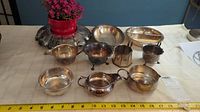 Set of eight EP silverware pieces including various bowls, dishes, creamer, and sugar bowl displayed on table with measuring tape for scale.