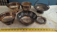 Set of five silver-plated bowls and dish arranged on a table with a measuring tape showing their size.