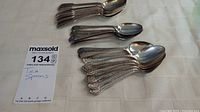 Top-down view of 18 stacked teaspoons with decorative handles on a white tablecloth.