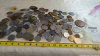 Wide view of a pile of tokens, medallions and coins spread out on a white surface with a measuring tape displaying approx 18 inches length