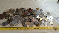 Wide view of a large assortment of various tokens and medallions spread on a surface with a ruler for scale.