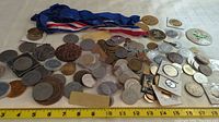 Wide view of multiple medallions, tokens, and coins spread out with a measuring tape showing size scale.