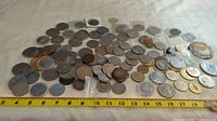 Wide view of assorted tokens and medallions laid out on white surface next to a measuring tape showing length of about 18 inches.