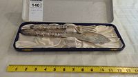 Full view of the fish serving set in its box next to a measuring tape showing length approximately 12 inches.