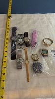 Top view showing all ten watches laid out on a white cloth with a measuring tape alongside for scale.