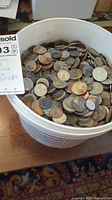 White plastic bucket filled with various international wishing well coins showing different colors and levels of tarnish.