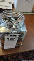 Plastic jar filled with assorted world coins from various countries, coins of different sizes and metals visible.