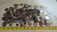 Photo of the assortment of coins spread out on a surface with a measuring tape showing approximately 13 inches in length, highlighting the quantity and variety in size and metal tone.