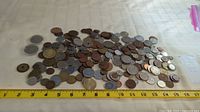 Wide view of the spread of assorted world coins placed next to a measuring tape showing approx 13 inch span