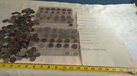 Photo shows a spread of various world coins both loose and in plastic holders, placed next to a measuring tape for scale.