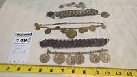 Five coin bracelets laid out with measuring tape for scale, showing overall size and coin detail.