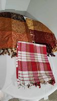 Three Turkish throws arranged with brown, orange, red, and yellow hues visible, showing patchwork and plaid patterns with fringed edges.