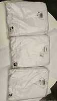 Three white microfiber bathrobes folded, showing labels with size XS and made in Turkey tag.