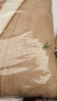 Brown embroidered luxury throw in plastic packaging with visible fabric texture and embroidery.