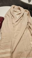 Full view of the beige Turkish bathrobe laid out showing its shawl collar, long sleeves, and front pockets.