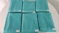 Six aquamarine towels individually bagged, laid out flat on a white surface.