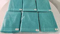 Photo top view of 6 aquamarine towels arranged side by side on a white surface, showing color and packaging.