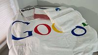 Google promotional oversized beach towel visible with partial colorful logo printed on white fabric, laid out flat showing large size and colors.
