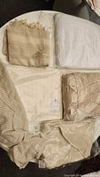 Photo showing six folded spa items laid flat including white waffle blanket, beige robe, pestemal towels, hooded towel, and spa cover up in neutral tones.