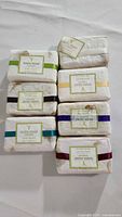 Seven bars of Napa Soap wrapped in white textured paper with different colored bands, laid out on a white surface.