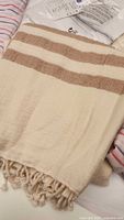 Close-up of natural cream colored Turkish pestemal towel with brown horizontal stripes and fringed edges.