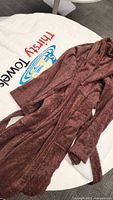 Brown plush bathrobe laid out showing shawl collar, belt, and pocket