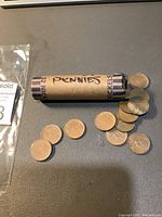 Image showing a paper roll labelled 'PENNIES' containing Canadian pennies with some coins scattered outside the roll. Coins display the Rock Dove design visible on some coins.
