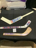 Three vintage mini hockey sticks displayed on black fabric, showing front side logos and graphics