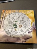 Front and back view of the 2016 Canadian $25 pure silver coin featuring an elf in a winter forest building a birdhouse, showing coin detail and background illustration.