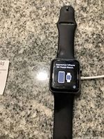 Apple Watch Series 2 38mm with black band and screen showing pairing instruction in French to approach iPhone.