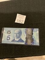 Front side of Canadian 5 dollar polymer banknote showing portrait of Sir Wilfrid Laurier, the number '5', maple leaf detail, and transparent security window