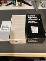 Top angle photo showing opened box filled with a full deck of white cards with a visible game instructions booklet/card beside it.