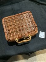 Closed view of woven rectangular picnic basket with handle and clasp on black cloth background.