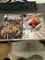 Photo showing two individually bagged comic books on a desk in front of a computer keyboard. Left comic is Clive Barker's Night Breed with horror-themed cover art. Right comic is Phantom Guard with a stylized red demon on cover.
