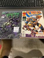 Photo showing two comic books side by side on a desk with keyboard in background. Left is Full Bleed's "Pitt" with dark monster cover, right is Marvel Comics' "Cable" issue #2 with character in yellow armor and robotic companion cover.