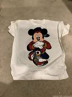 White cotton T-shirt with large colorful Mickey Mouse graphic on the front, laid flat on the floor.