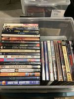 Top view of approximately 26 DVDs arranged in a plastic bin showcasing various movie titles on spines