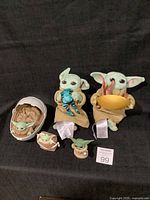 Full set of five Grogu-themed items from Star Wars: The Mandalorian displayed on black background. Two plush Grogu figures in robes holding small companion toys and three smaller Grogu figures including one in a cracked pod cradle.