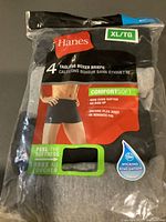 Four-pack of black Hanes tagless boxer briefs in sealed packaging with ComfortSoft fabric and moisture-wicking feature, size XL/TG.