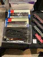Plastic container with assorted HO scale model railroad track pieces including switches, curves, and straights, alongside boxed Walthers passenger train cars.
