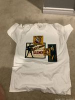 White Jantzen T-shirt with vintage style Faust Brand Salmon label graphic print laid flat on carpet.