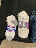 White athletic Cooper socks with gray heel and toe, and white Spalding socks grouped with three pairs of fuzzy Hot Steps socks in different colors on black surface