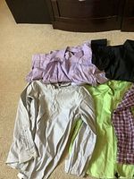 Overview of nine men's large dress shirts in assorted colors and patterns lying on floor including purple stripe, black, white, beige, lime green, and red checkered patterns