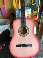 Front view of full size 6-string acoustic guitar in pink sunburst finish showing body and neck against pegboard background