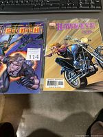 Two comic books, Sci-Tech and Hawkeye, placed side by side on a surface with keyboard in background. Both are in bagged sleeves, front covers visible.